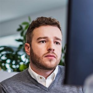 Oskar Oldorf, a white man in his 30s with curly brown haid and a short beard sitting in front of a half-visible pc screen looking serious.